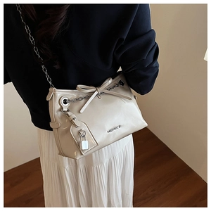 Detail view of cream-colored shoulder bag featuring chain strap and bow decoration