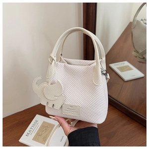 Detail of cream woven bucket bag with smooth leather handle and cute elephant charm
