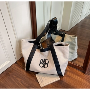 Detail of large canvas tote bag with black leather straps and embroidered logo