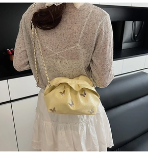 Pale yellow pleated bucket bag with silver butterfly charms shown on model's shoulder