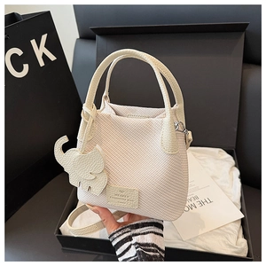 Detail of cream woven bucket bag featuring elephant charm and leather top handle