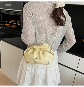 Detail of cream yellow pleated bucket bag with silver butterfly charms and chain strap