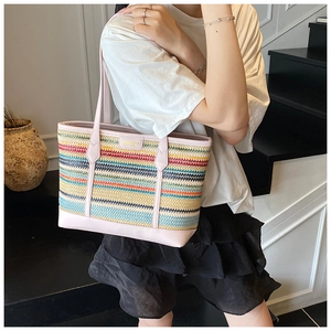 Detail of colorful striped straw tote bag with pink leather handles worn by a model