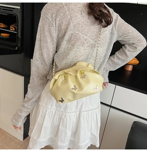 Detailed view of yellow pleated cloud bucket bag with silver butterfly charms on chain strap