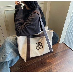 Detail of a large canvas tote bag with brown leather trim and NO GO logo on front