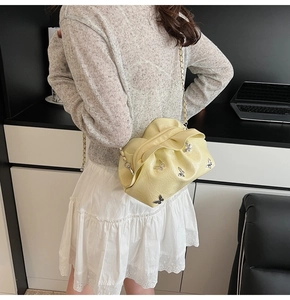 Detail of a light yellow pleated bucket bag featuring silver butterfly accents and chain strap