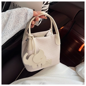 Detail of beige textured bucket bag with an elephant charm in a car lifestyle setting