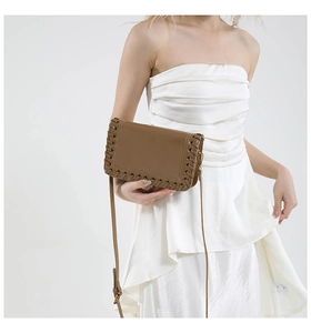 Detail of woven cross-lace stitching on brown leather shoulder bag with sleek flap