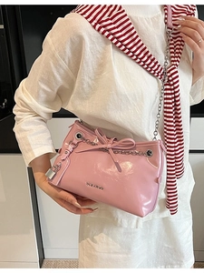 Pink patent leather underarm bag with silver chain and bow detail shown on a model
