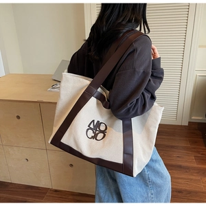 Detail of a large beige canvas tote bag with leather trim and MOC CO embroidery logo