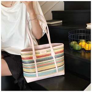 Rainbow woven straw tote bag with pink leather trim shown on steps in summer scene