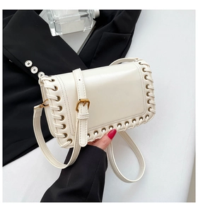 Detailed view of woven edge trim and gold metal buckle on a cream shoulder bag