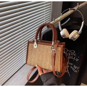 Close-up of woven straw handbag with brown leather strap and braided handle detail
