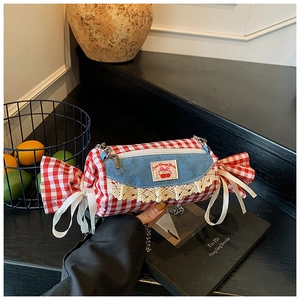 Detail of candy-shaped plaid crossbody bag with denim flap and lace trim on a table