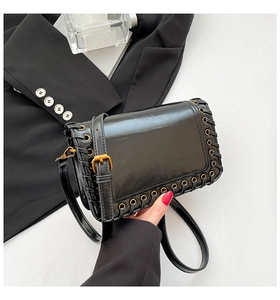 Detail view of black glossy leather bag with woven metal eyelets and golden buckle strap