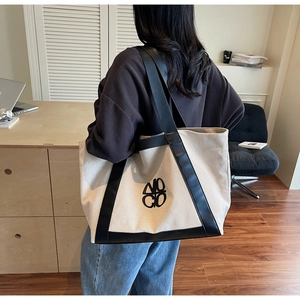 Detail of a large canvas tote bag showing the MOCO logo and black leather contrast trim