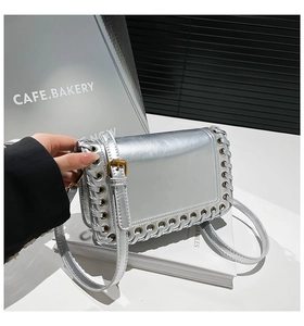 Detail of silver metallic textured crossbody bag with metal eyelets and woven leather edges