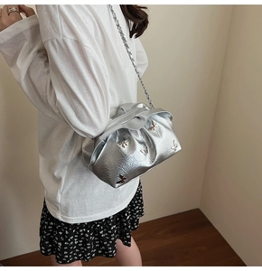 Detail view of silver pleated bucket bag with decorative butterfly patches and chain strap