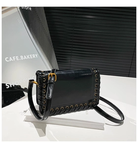 Detail of a black leather square bag featuring gold eyelets and braided cord decoration