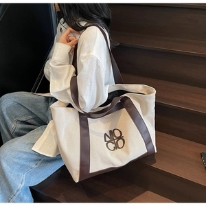 Detail of large canvas tote bag showing cream fabric with brown leather trim and logo
