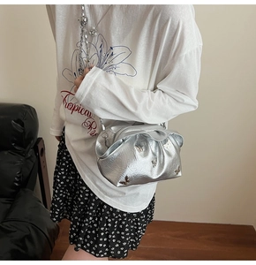 Detail of silver pleated bucket bag featuring metallic butterfly charms and a thick chain strap