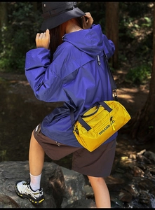 Outdoor close-up of a bright yellow nylon cylinder crossbody bag with black handle straps