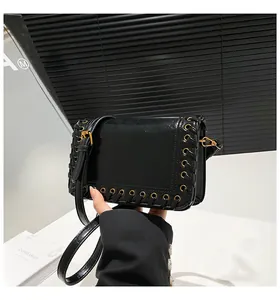 Detail of black glossy shoulder bag with gold metal eyelets and woven leather accents