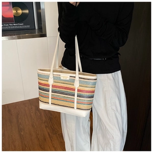 Detail of multi-color woven tote bag with white leather handle and designer logo patch