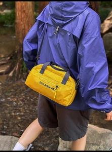 Outdoor shot of a yellow nylon sports duffle bag with black straps and brand lettering