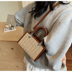 Detailed view of woven straw crossbody bag with brown leather trim and metal hardware