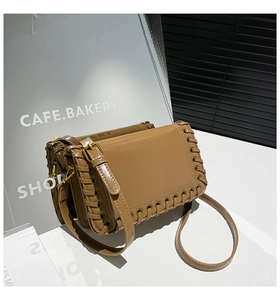 Detailed view of khaki shoulder bag with woven leather trim and golden metal buckles