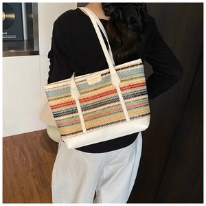Detail of colorful woven straw tote with white leather trim and brand name plaque