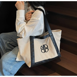 Close-up of off-white canvas tote bag with black leather handles and NOCO embroidery