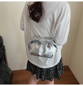 Silver bucket bag with 3D butterfly details and chain strap shown on model's shoulder