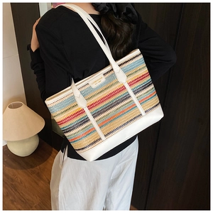 Detailed side view of a large multi-colored woven straw tote bag worn by a model