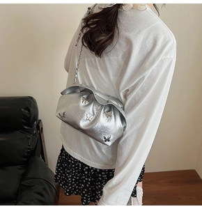 Detail showing metallic silver pleated bucket bag with decorative butterfly accents and chain