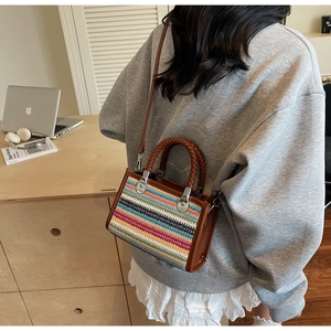 Detailed close-up of rainbow woven striped handbag with brown leather trim and metal hardware