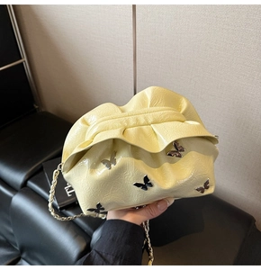 Close-up of pale yellow pleated bucket bag featuring silver butterfly metal studs and chain