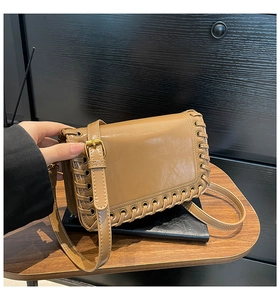 Detail of woven brown crossbody bag showing adjustable strap and golden buckle hardware