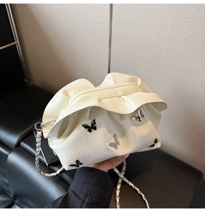 Detailed macro view of the cream pleated bucket bag with glossy finish and butterfly charms