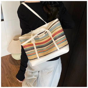 Close-up of a colorful woven straw tote bag with white faux leather trim and handle details