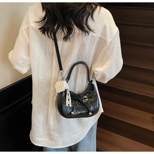 Détail d'un sac à main en cuir verni noir avec nœud et perles porté par un mannequin