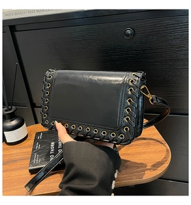 Detail of black woven leather shoulder bag with metallic eyelets and gold hardware closure