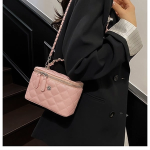 Détail d'un sac vanity rose matelassé avec bandoulière en cuir et chaîne sur blazer noir