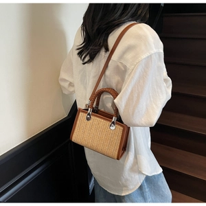 Detail of woven straw handbag with brown leather trim and braided handle shown on model