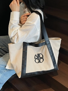 Large beige canvas tote bag with black leather trim and NOGO logo carried by a model