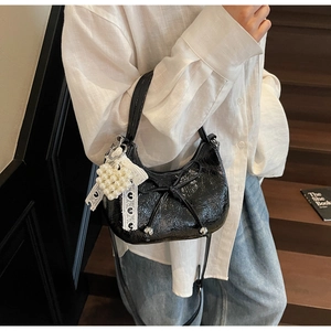 Détail du sac croissant noir brillant avec pendentif cœur perlé et nœud décoratif