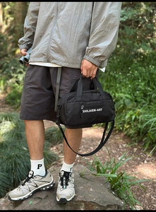 Detail of durable black nylon crossbody bag featuring reinforced handles and side zippers