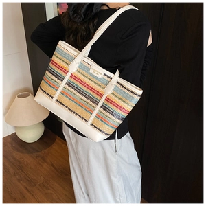 Detail of colorful woven straw tote bag with white leather straps and brand logo plaque