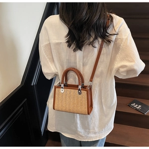 Detail of straw woven handbag with brown leather trim and silver metal rivets on bag